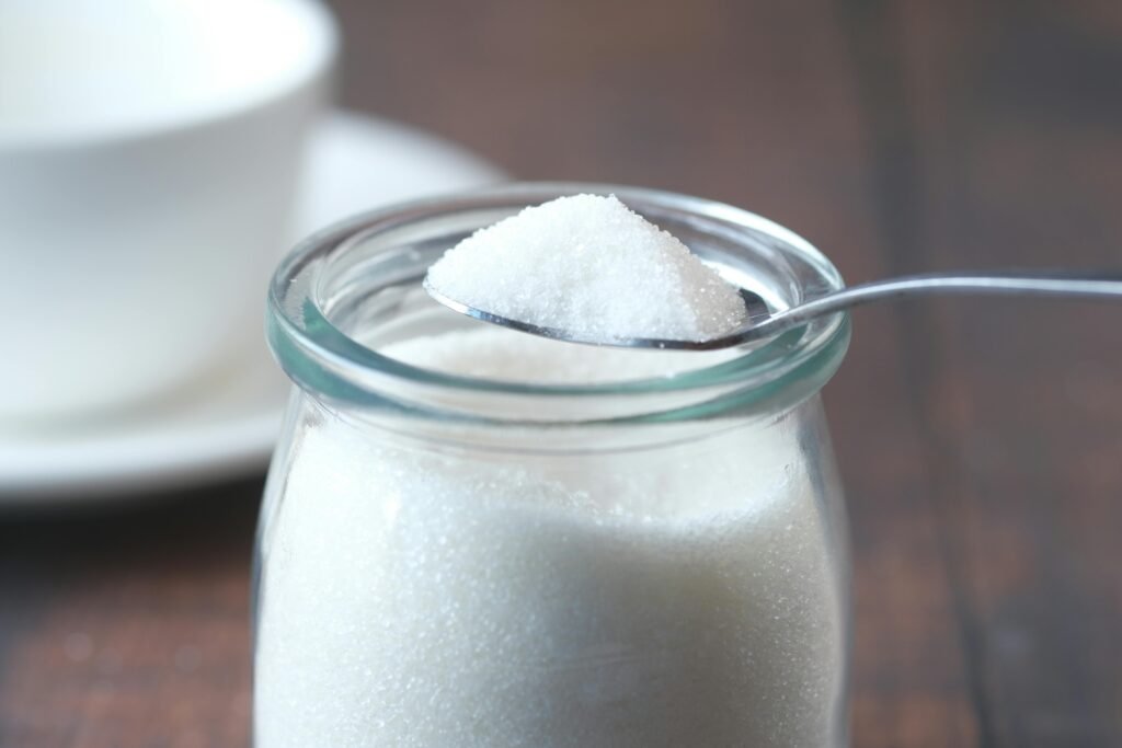 A close-up shot of white sugar in a glass jar, delicately scooped with a spoon. Ideal for food concepts.