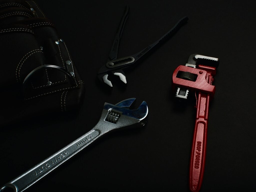 Close-up of various hand tools including wrenches and pliers on a dark surface.