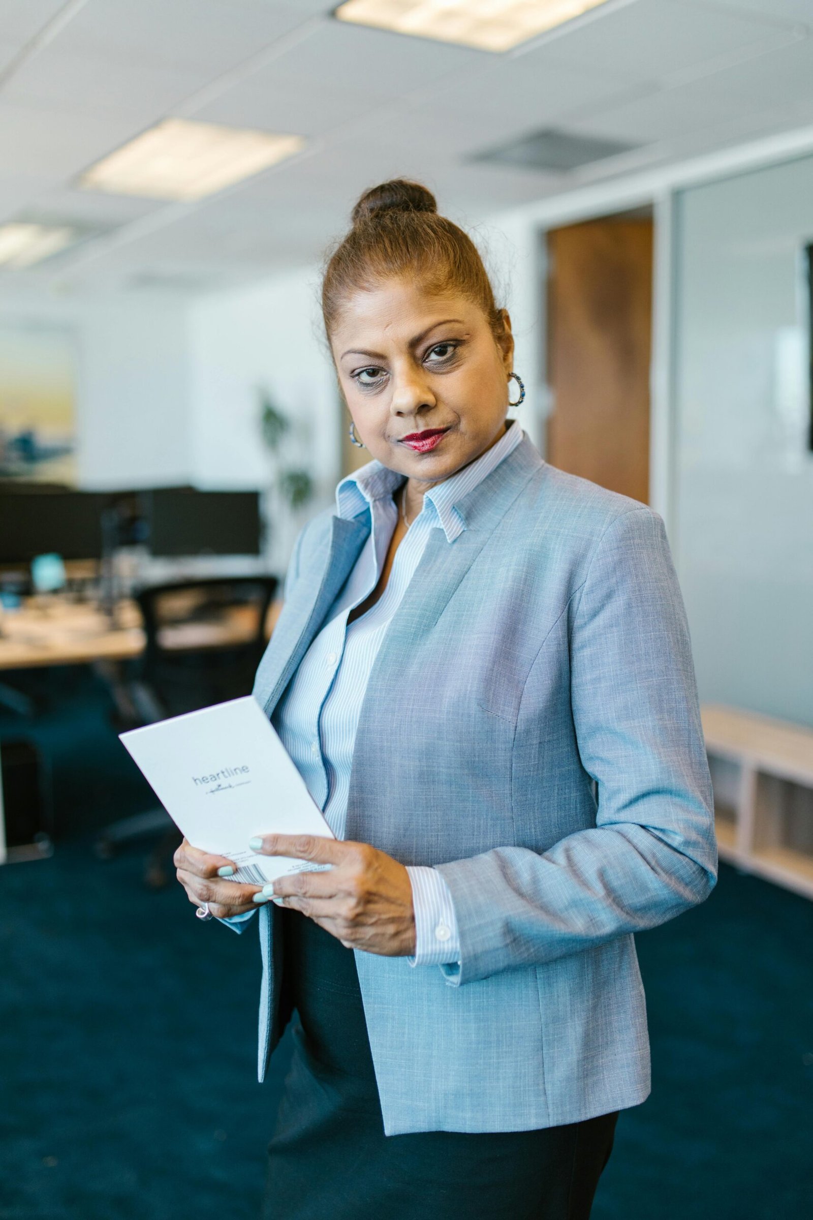 Confident businesswoman in office holding a document, showcasing professionalism and leadership.