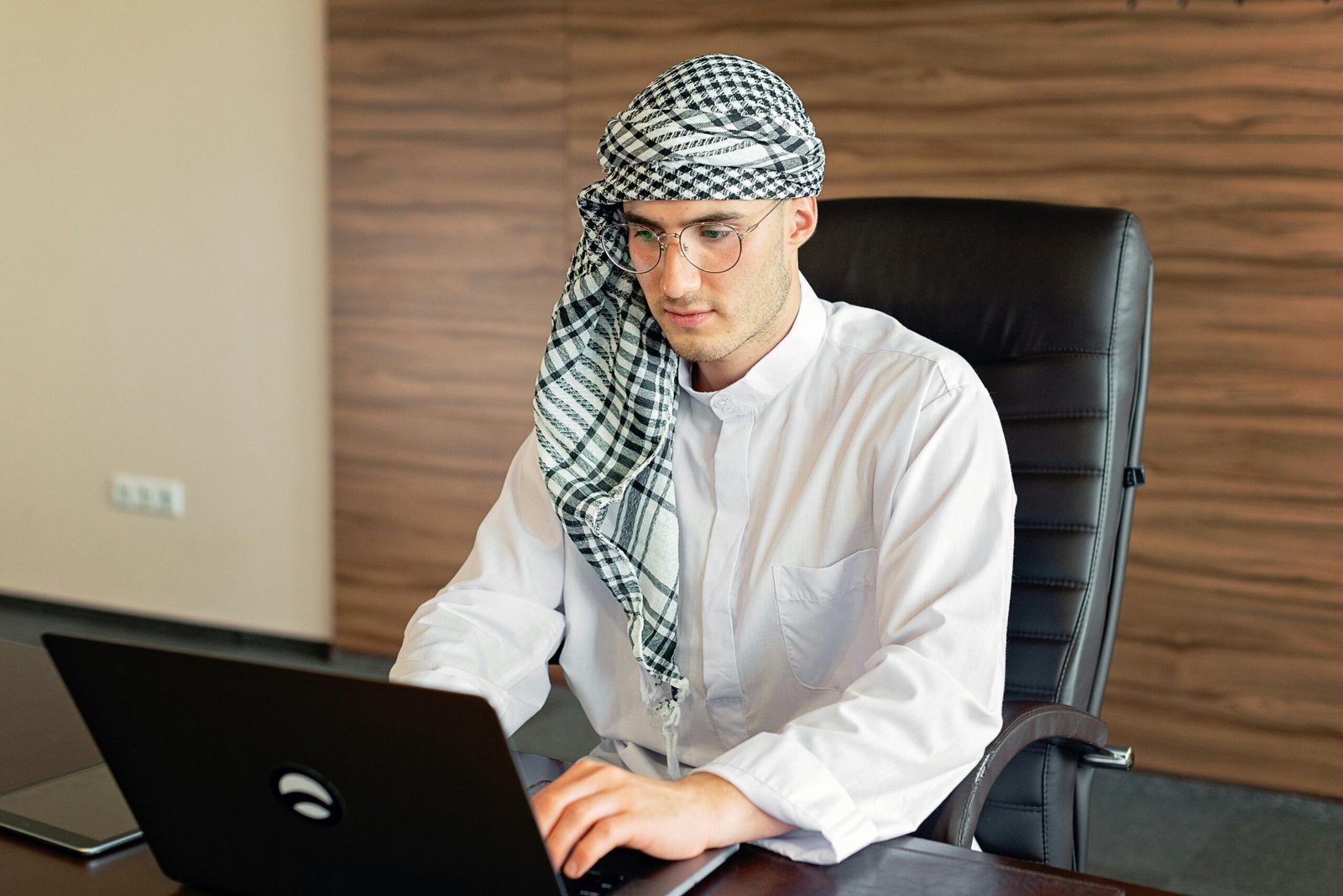 Middle Eastern man in traditional attire working on a laptop in an office setting.